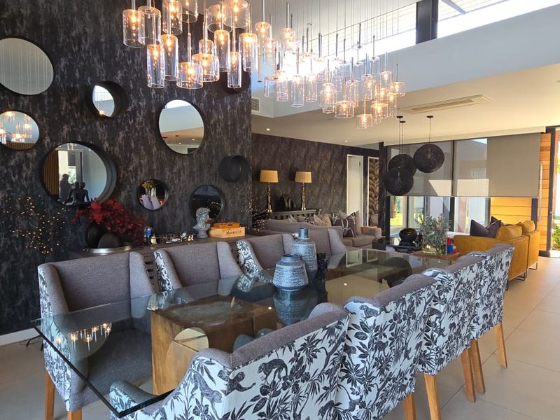 Spacious open-plan living and dining area featuring modern tiled floors, high ceilings with statement pendant lighting, and large sliding doors leading to the patio.
