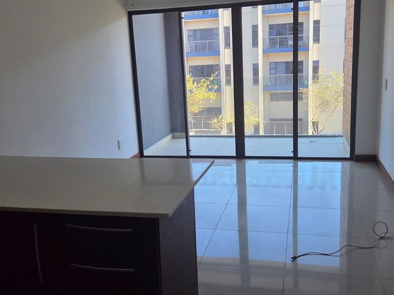 Modern open-plan living area featuring a kitchen island with stone countertops, sleek tiled flooring, and large sliding glass doors leading to a balcony.