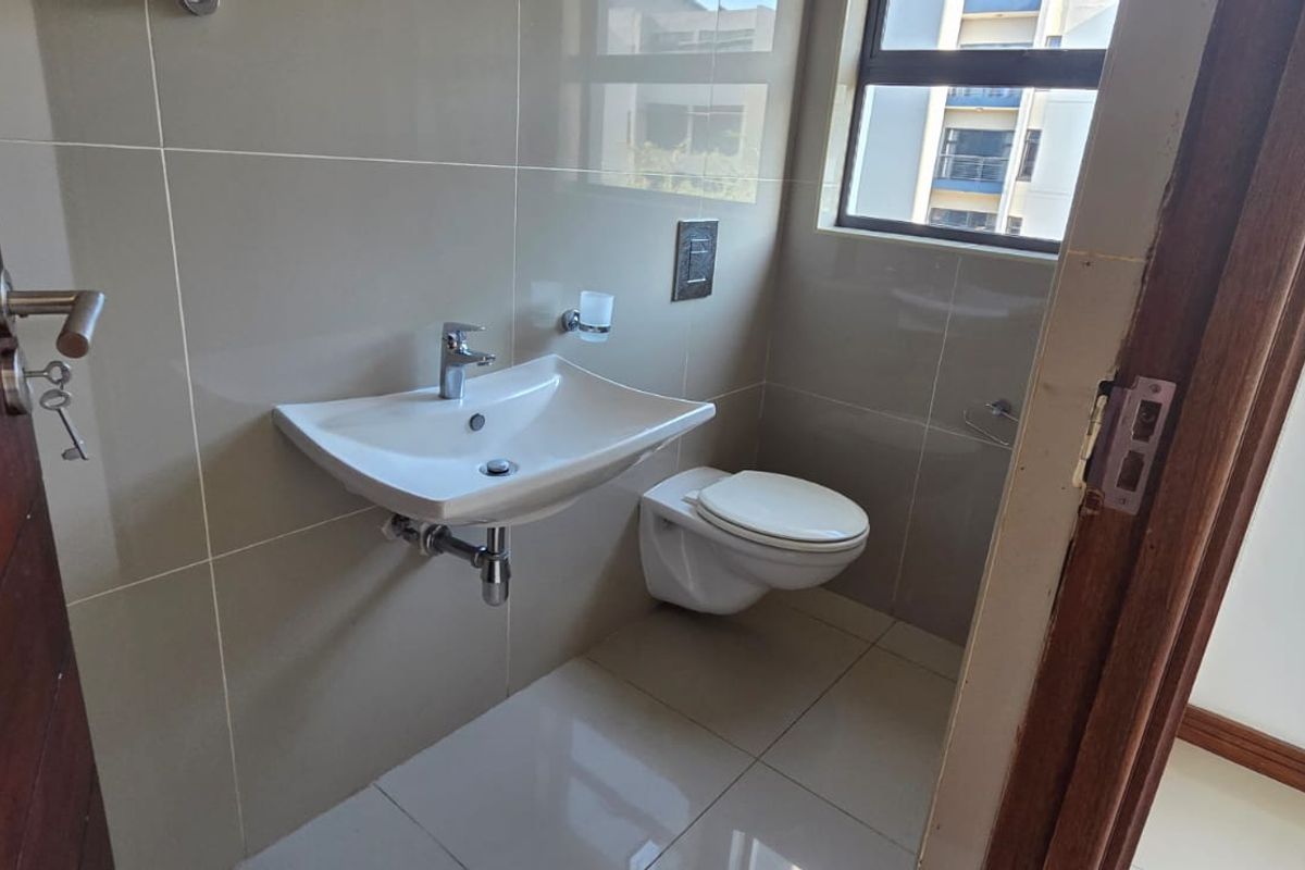A modern, compact guest bathroom featuring a wall-mounted basin and wall-hung toilet with neutral ceramic tiling throughout.