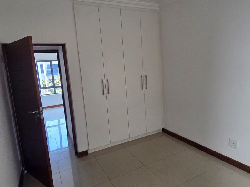 A clean, empty bedroom featuring neutral tiled flooring and white built-in cupboards, offering a blank canvas for personalization.