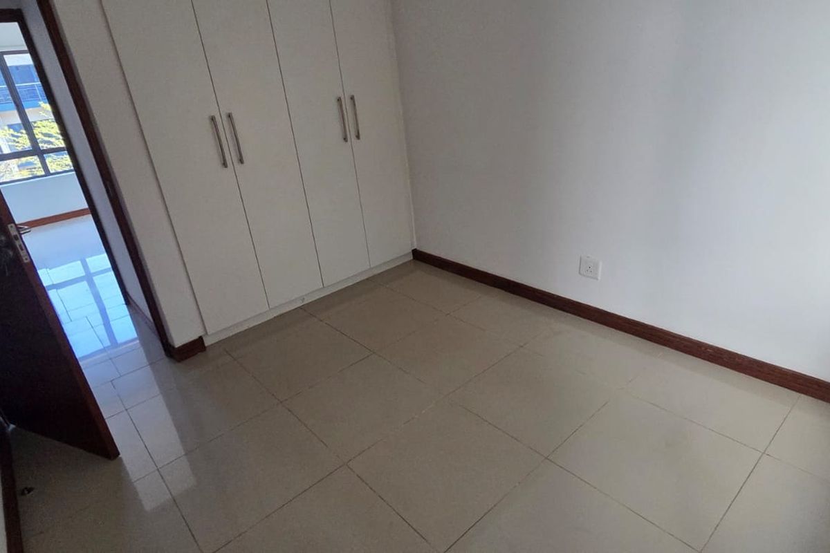 A clean, empty bedroom featuring neutral tiled flooring and built-in cupboards, offering a versatile space ready for personalization.