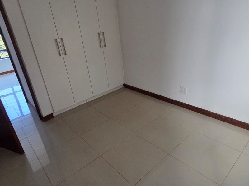 A clean, empty bedroom featuring neutral tiled flooring and built-in cupboards, offering a versatile space ready for personalization.