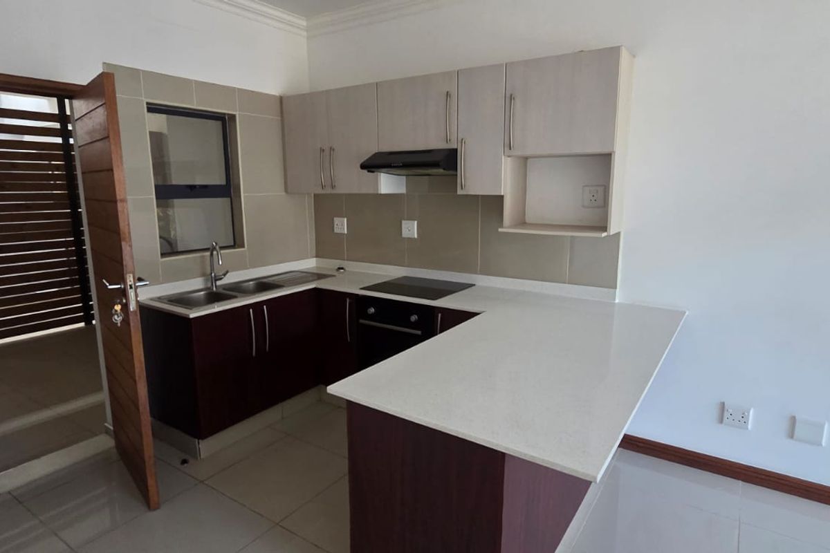 A modern, empty kitchen featuring dark wood cabinetry, light quartz countertops, a built-in electric hob, oven, and extractor fan with tiled finishes.