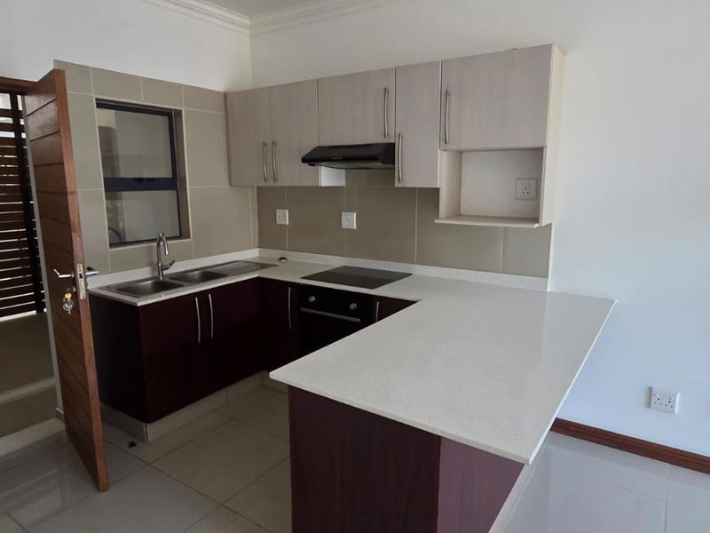 A modern, empty kitchen featuring dark wood cabinetry, light quartz countertops, a built-in electric hob, oven, and extractor fan with tiled finishes.