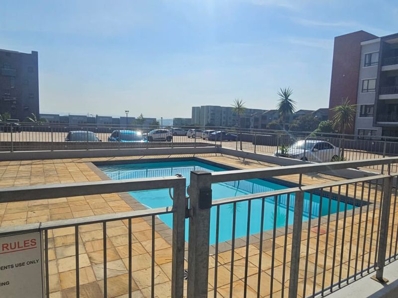 Communal swimming pool area featuring paved decking and secure metal perimeter fencing within an apartment complex.