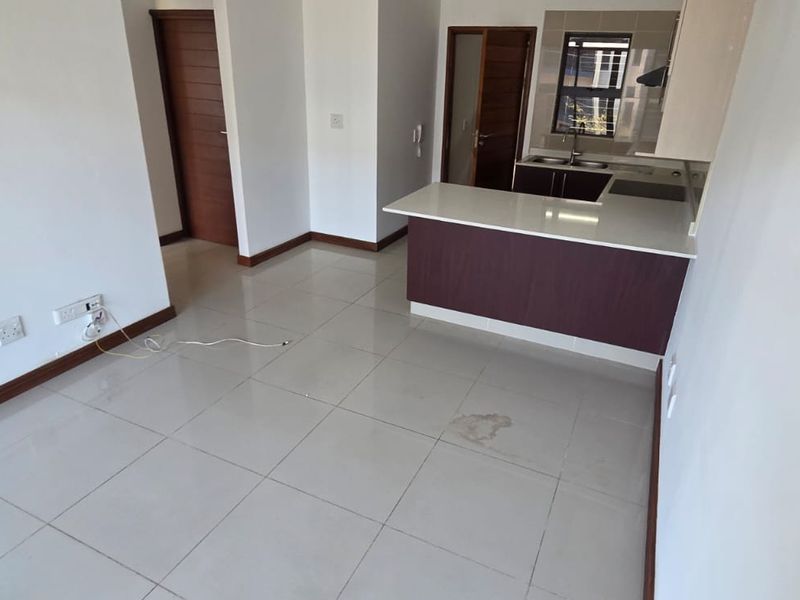 An open-plan living and kitchen area featuring tiled flooring, modern cabinetry, and a breakfast bar, presented in a clean, vacant condition.