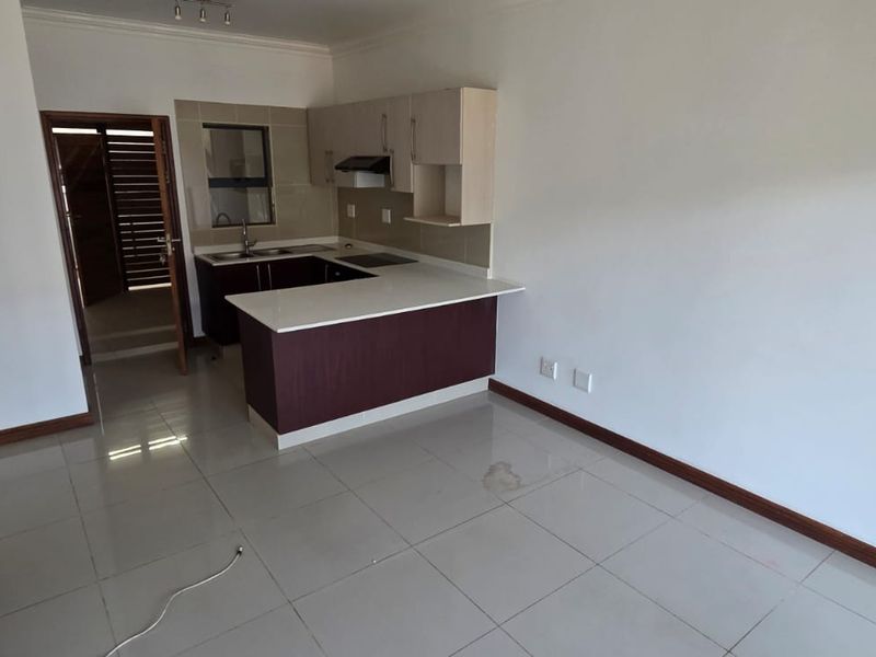 An open-plan living and kitchen area featuring tiled flooring, built-in cabinetry with laminate countertops, and an integrated extractor fan.