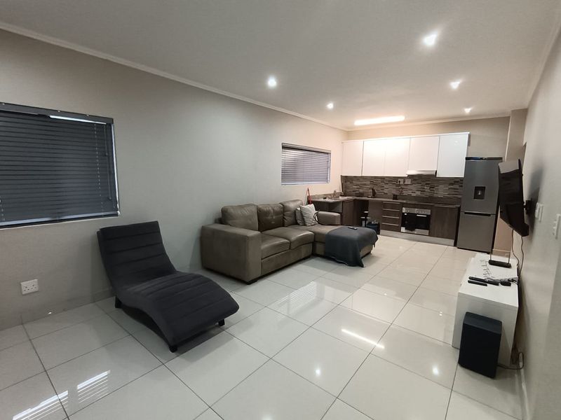 Open-plan living area featuring tiled floors, recessed lighting, and a modern kitchen with built-in cabinetry, oven, and extractor fan.