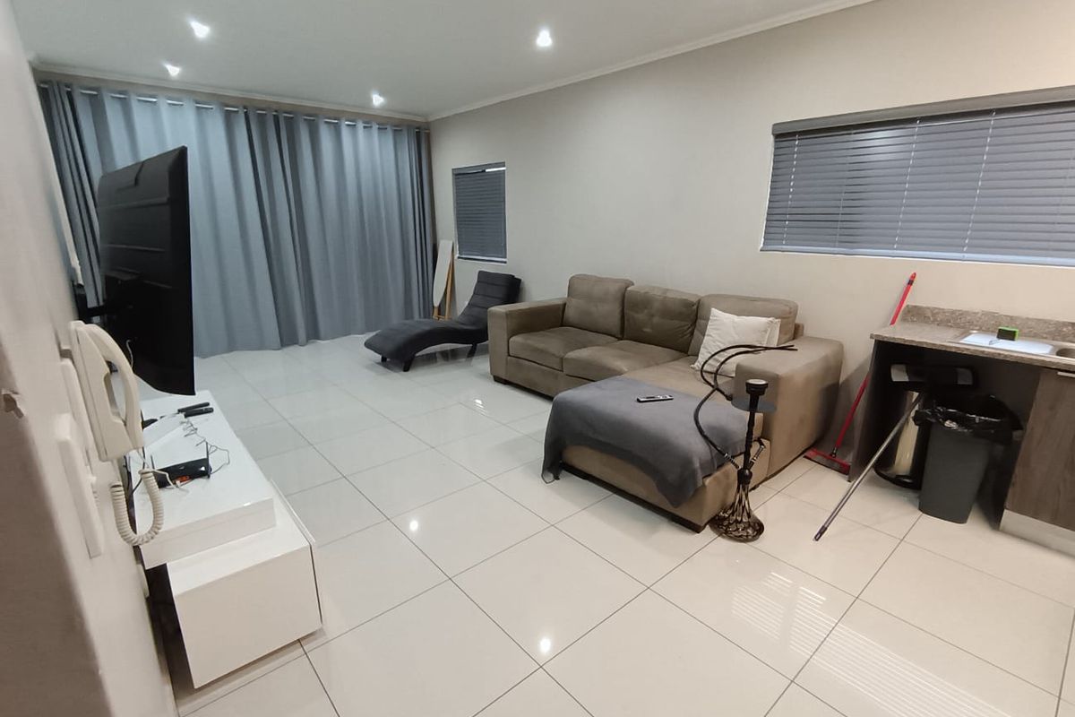 Spacious living area featuring large format floor tiles, recessed downlighting, and a compact built-in kitchenette counter with integrated sink.