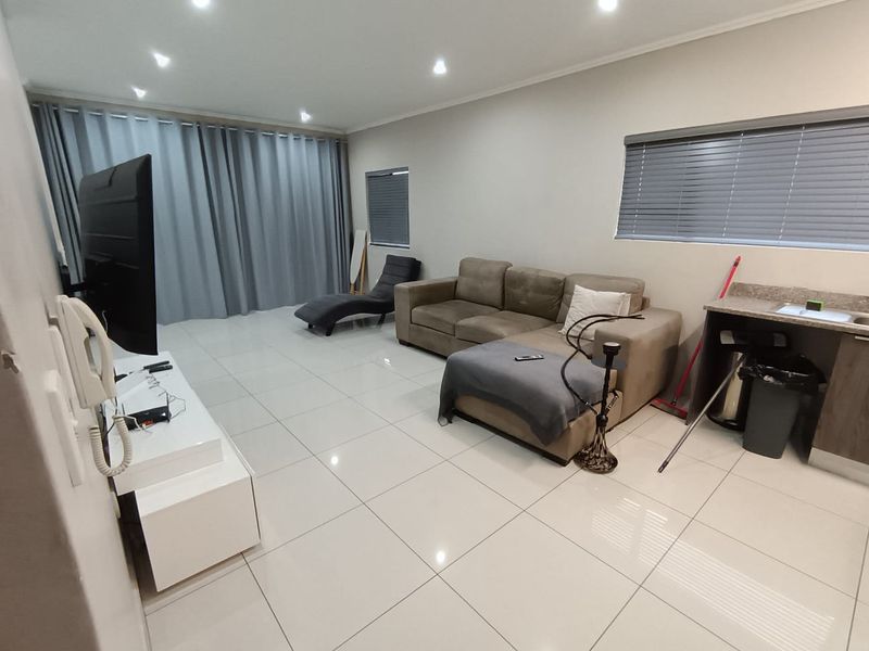 Spacious living area featuring large format floor tiles, recessed downlighting, and a compact built-in kitchenette counter with integrated sink.