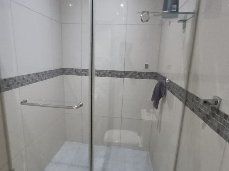 A clean, modern walk-in shower featuring a glass enclosure, neutral wall tiles with a decorative mosaic border, and recessed ceiling lighting.