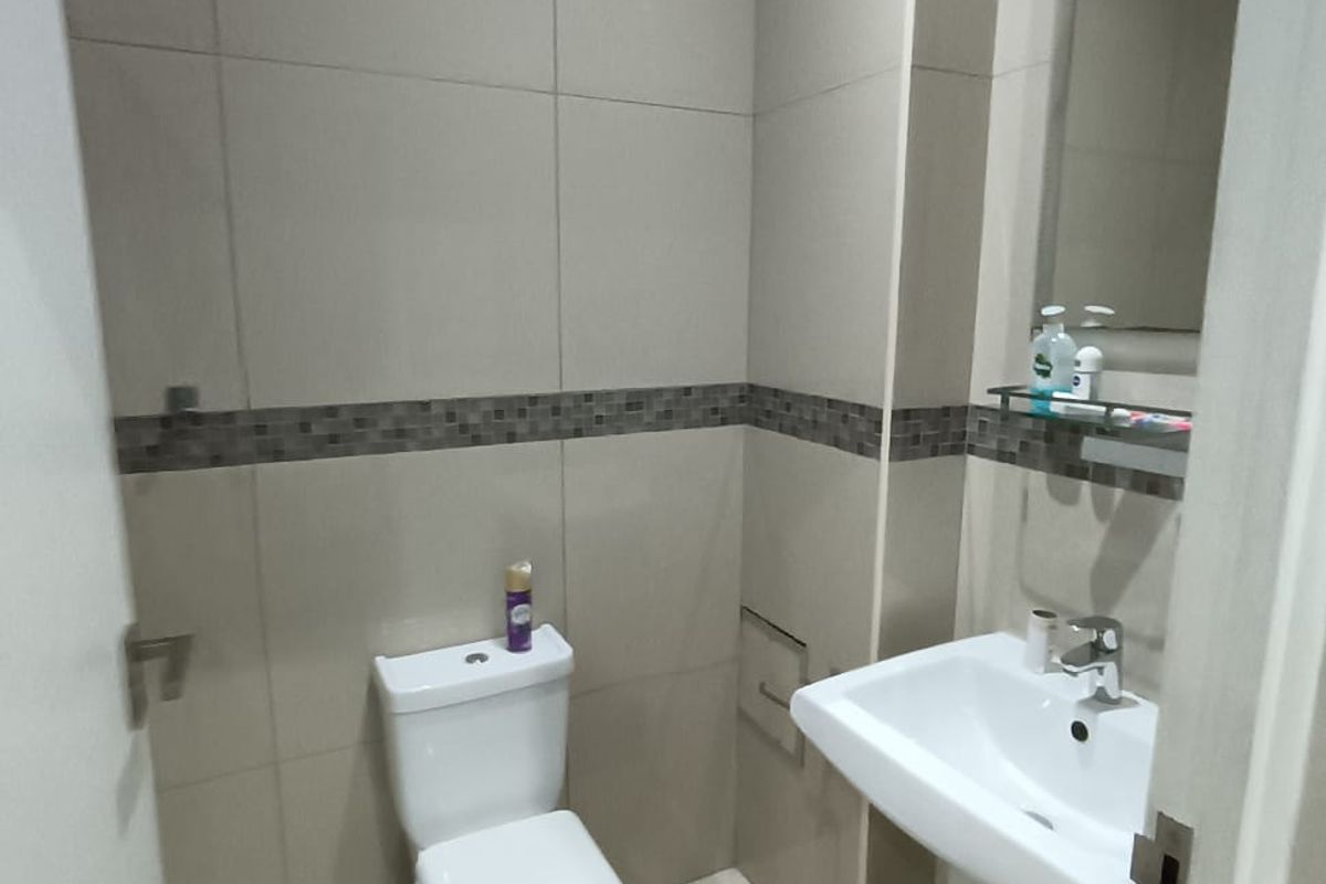 A compact, modern bathroom featuring neutral wall tiles, a pedestal washbasin, and a standard toilet.