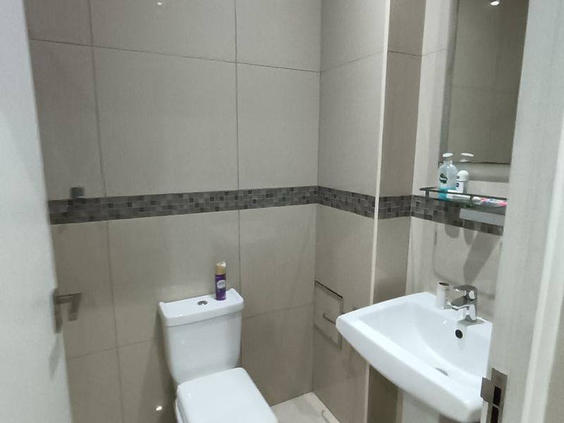 A compact, modern bathroom featuring neutral wall tiles, a pedestal washbasin, and a standard toilet.