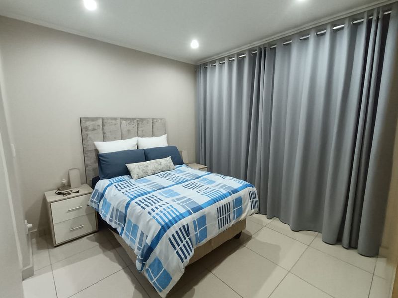 A well-maintained bedroom featuring neutral tiled flooring, recessed ceiling lighting, and full-length window curtains.
