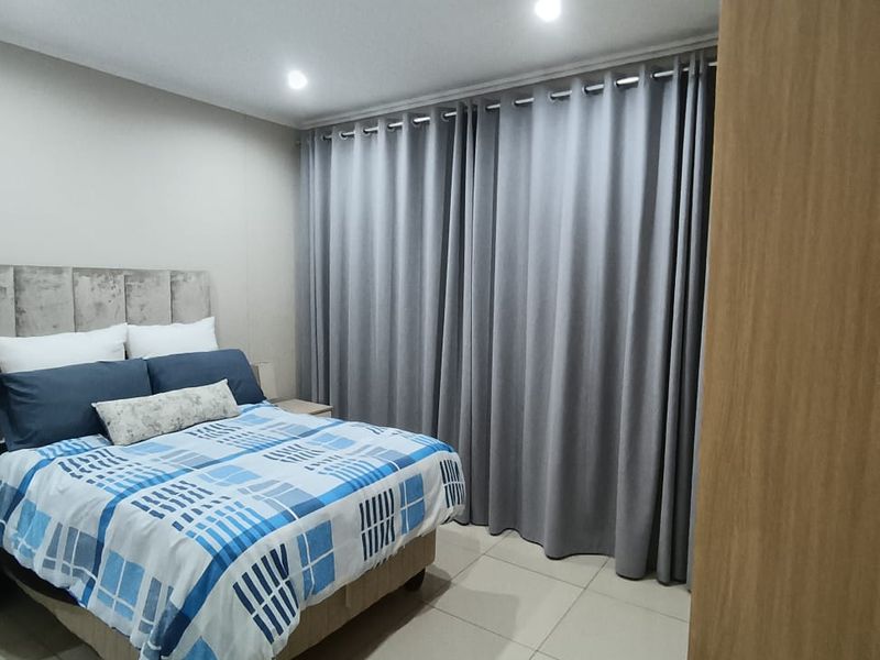 A well-maintained bedroom featuring neutral tiled flooring, recessed ceiling lighting, and full-length window curtains.