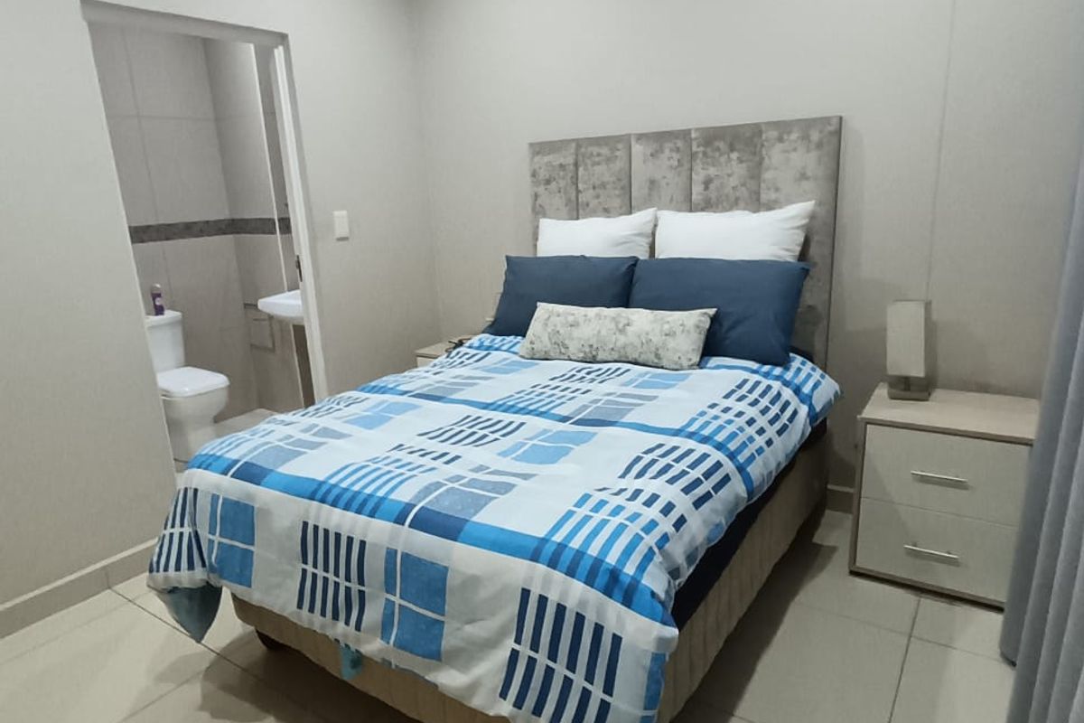 A well-maintained bedroom featuring neutral tiled flooring, recessed lighting, and an adjoining en-suite bathroom.