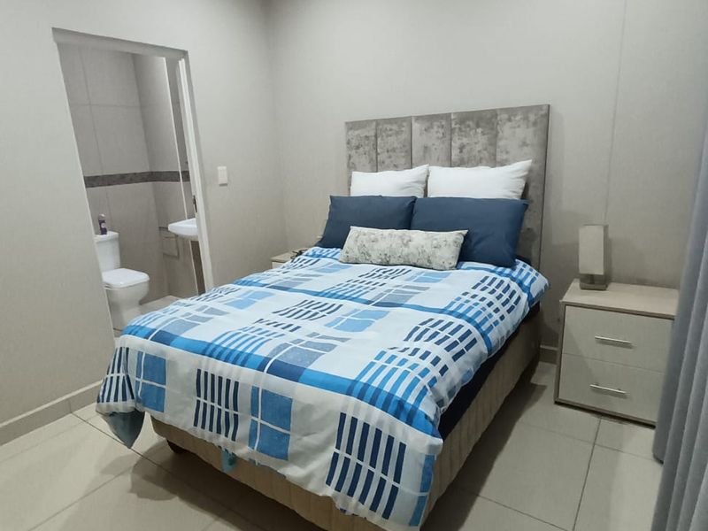A well-maintained bedroom featuring neutral tiled flooring, recessed lighting, and an adjoining en-suite bathroom.