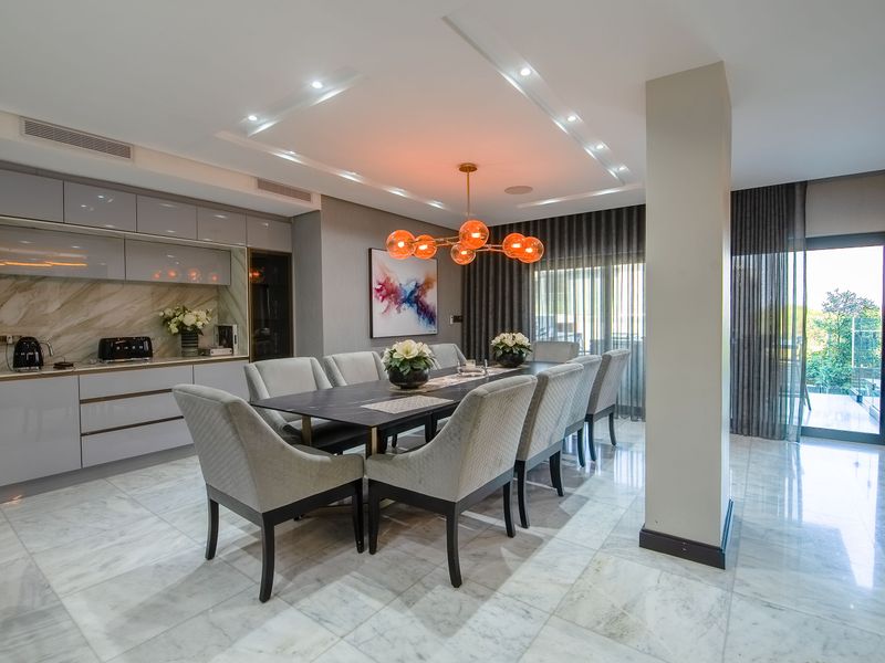 Modern open-plan dining area featuring polished marble flooring, recessed ceiling lighting, built-in cabinetry, and seamless access to an outdoor patio through sliding glass doors.