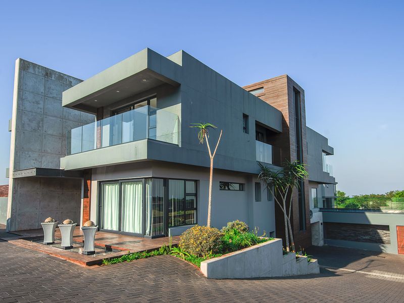 Modern multi-story architectural home featuring a striking combination of concrete, timber cladding, and glass balustrades with a paved driveway and landscaped entrance.