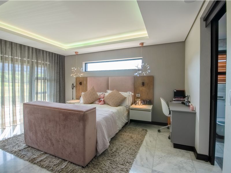 Modern bedroom featuring marble flooring, recessed cove lighting, a built-in headboard with floating nightstands, and direct access to an outdoor area via sliding doors.