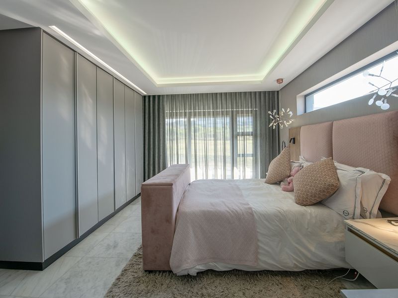 Modern bedroom featuring extensive built-in wardrobes, elegant cove lighting, marble-look flooring, and a horizontal clerestory window providing natural light.