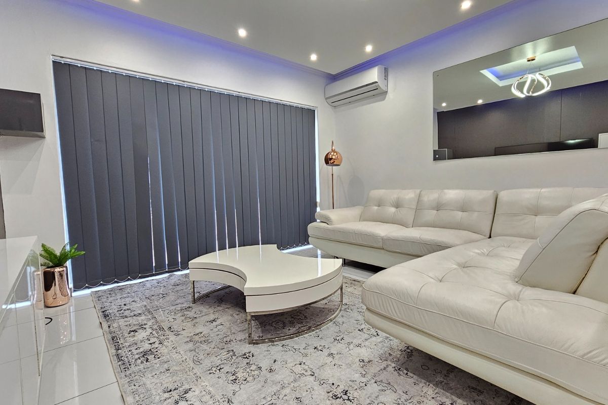 A modern, well-maintained living room featuring tiled floors, recessed downlighting, cove lighting, and a wall-mounted split-system air conditioner.