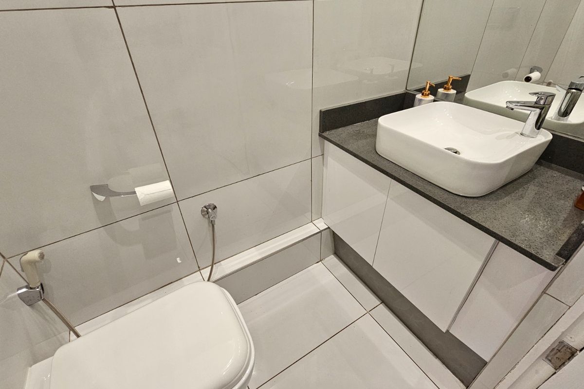 Modern bathroom featuring a wall-mounted toilet with bidet spray, a sleek vanity with stone countertop, vessel sink, and large wall mirror.