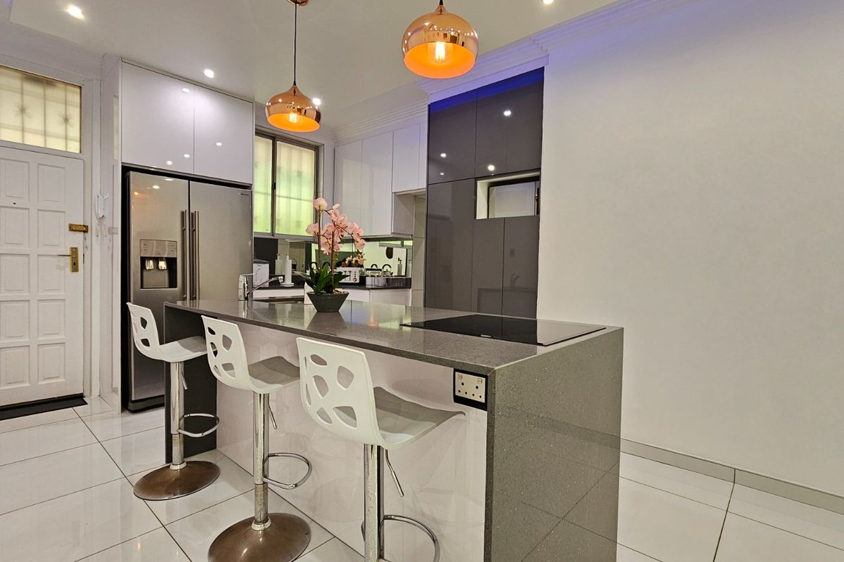 Modern kitchen featuring a stone-topped island with integrated cooktop, glossy cabinetry, and contemporary pendant lighting, set against polished tiled floors.