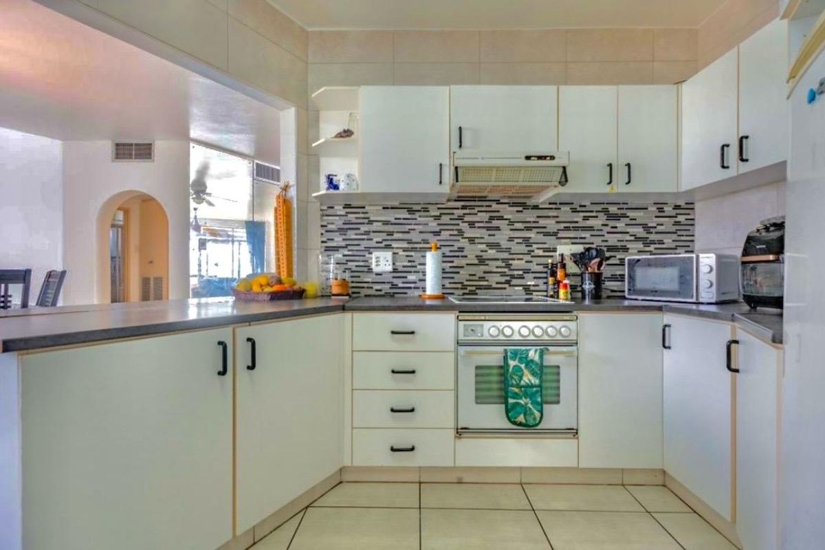 A functional kitchen featuring white cabinetry, mosaic tile backsplash, laminate countertops, and integrated cooking appliances, with an open-plan layout connecting to the living area.