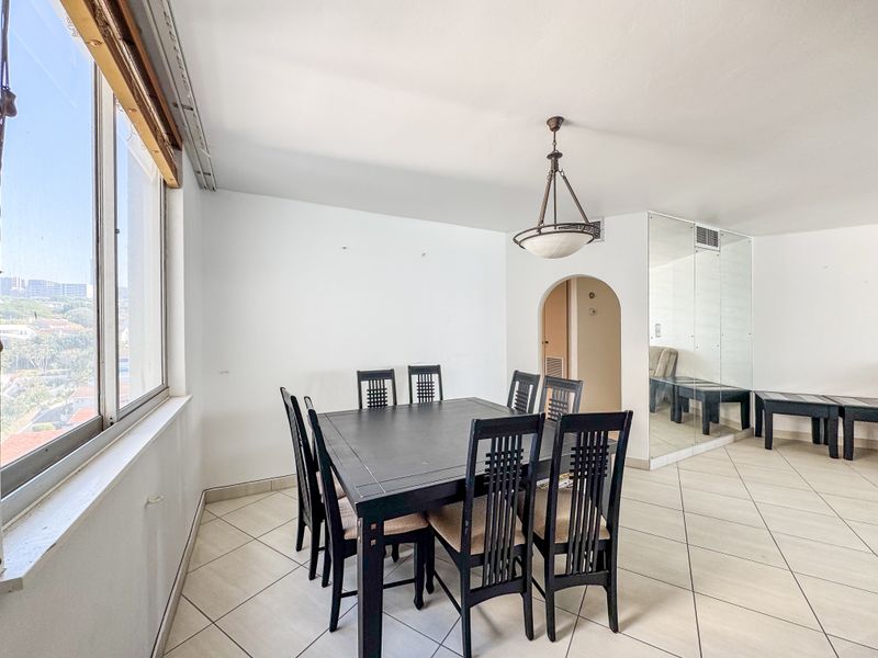 Dining area featuring tiled flooring, an arched entryway, mirrored wall accents, and a large window providing natural light and exterior views.