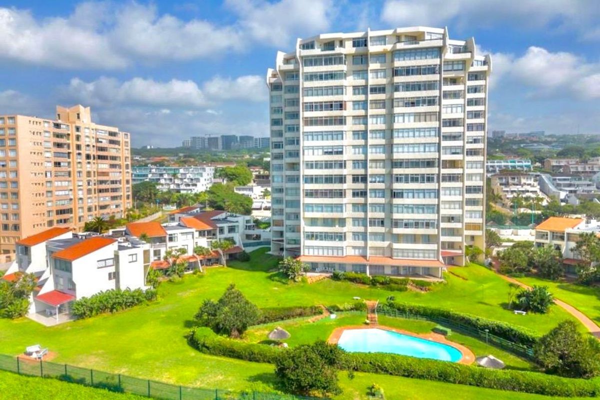 Aerial view of a multi-story apartment complex featuring landscaped grounds, a swimming pool, and surrounding residential neighborhood.