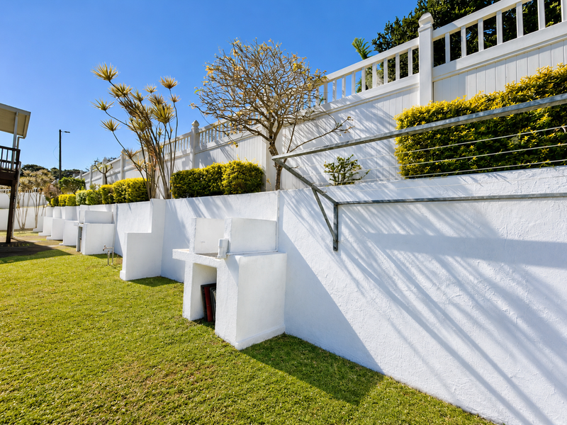 A well-maintained garden area featuring a white retaining wall with built-in masonry braai stations and a white picket fence boundary.