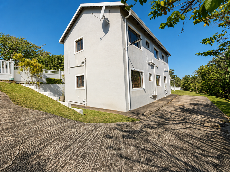 Rear view of the two-story house featuring a concrete driveway, white exterior walls, and a landscaped garden area with retaining walls.