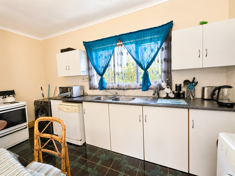 Functional kitchen featuring white cabinetry, laminate countertops, double sink, and tiled flooring, offering a practical layout with space for major appliances.