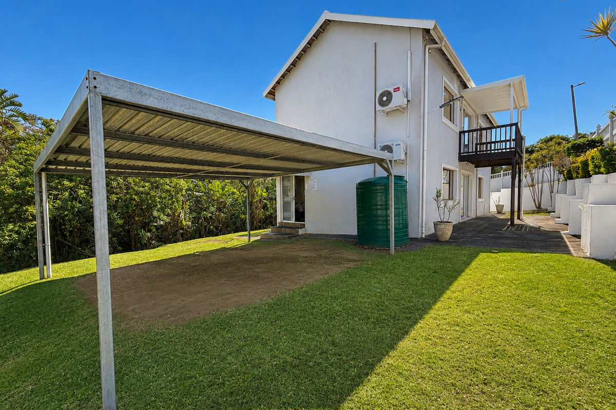 Rear view of the property featuring a metal carport, green water storage tank, split-system air conditioning units, and an elevated balcony.