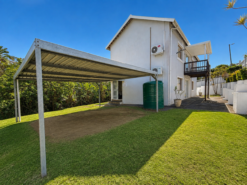 Rear view of the property featuring a metal carport, green water storage tank, split-system air conditioning units, and an elevated balcony.