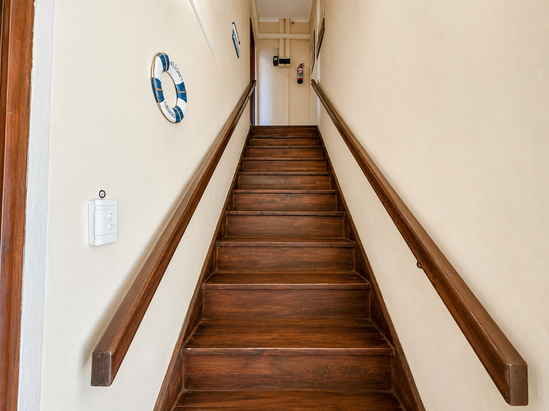 A straight wooden staircase with matching handrails leading to an upper level, featuring a wall-mounted fire extinguisher.