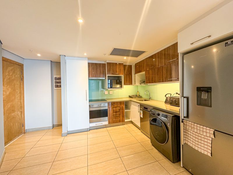 Modern kitchen featuring wood-grain cabinetry, integrated appliances, sleek glass splashback, and tiled flooring with recessed lighting.