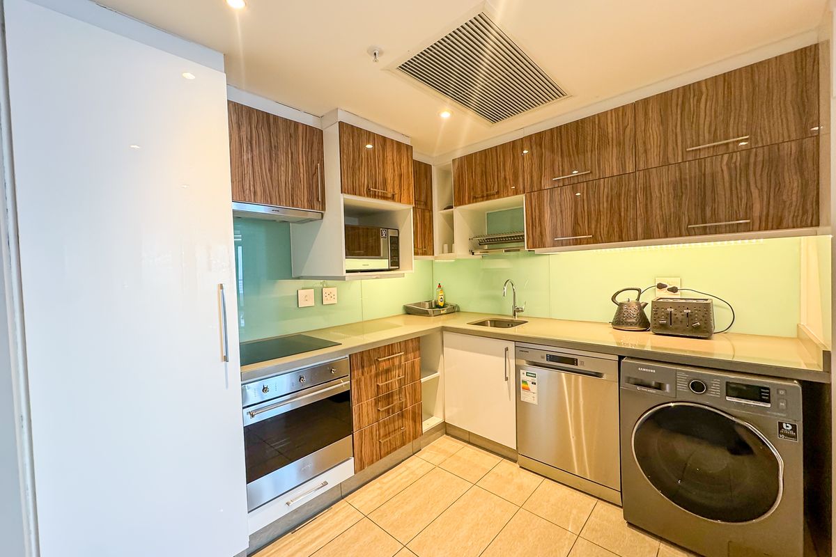 Modern kitchen featuring wood-grain cabinetry, glass splashback, integrated appliances, built-in oven, hob, and tiled flooring with recessed lighting.