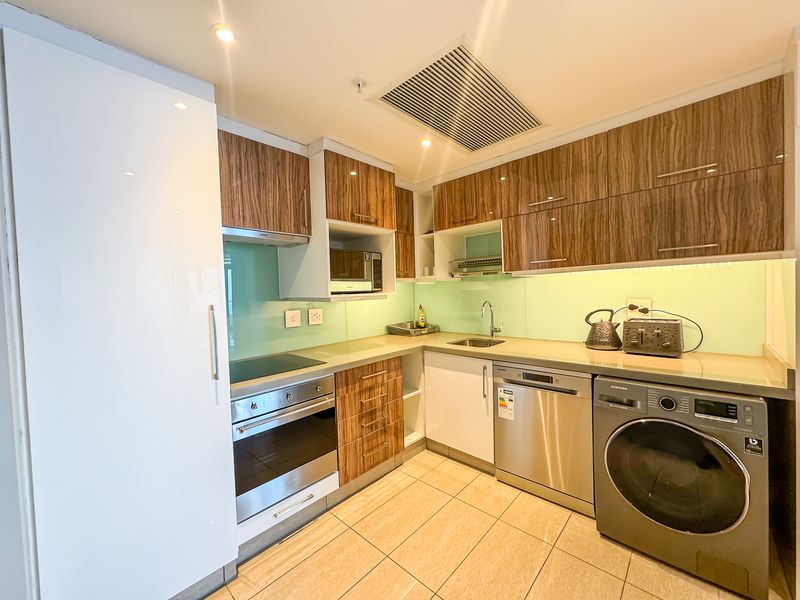 Modern kitchen featuring wood-grain cabinetry, glass splashback, integrated appliances, built-in oven, hob, and tiled flooring with recessed lighting.