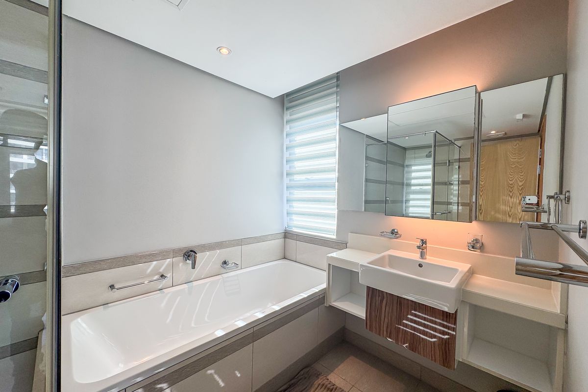 Modern bathroom featuring a built-in bathtub, wall-mounted basin with vanity storage, mirrored cabinetry, and neutral tiling throughout.