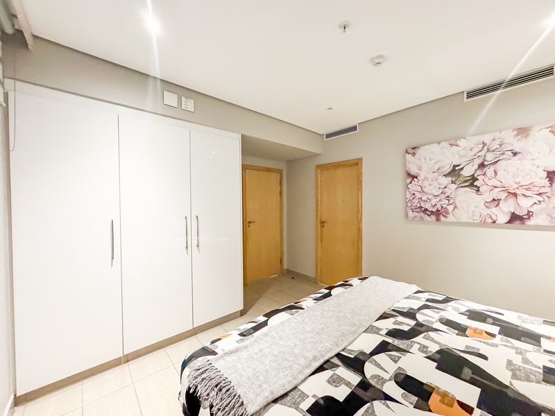 A well-maintained bedroom featuring built-in white wardrobes, tiled flooring, and integrated ducted air conditioning.