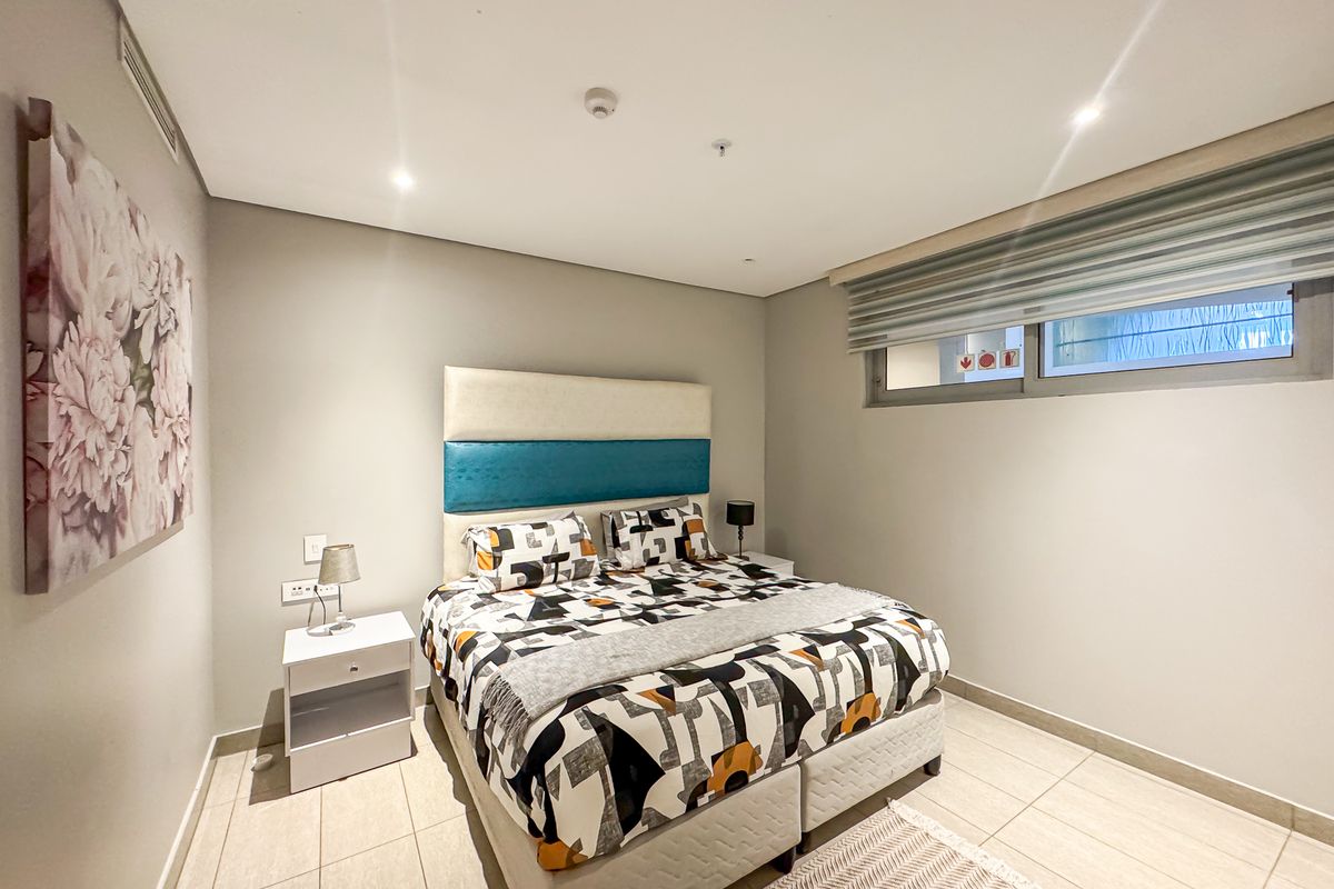 A well-maintained bedroom featuring neutral tiled flooring, recessed lighting, and a modern window with roller blinds.