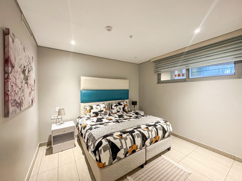 A well-maintained bedroom featuring neutral tiled flooring, recessed lighting, and a modern window with roller blinds.