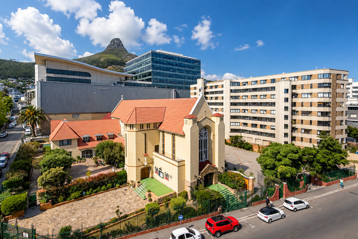Aerial view of the property complex featuring a historic building with a tiled roof, paved driveway, and surrounding landscaped gardens in an urban setting.