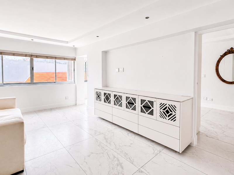 Bright and spacious living area featuring modern marble-look floor tiles, recessed ceiling lighting, and custom built-in cabinetry with a clean, minimalist aesthetic.