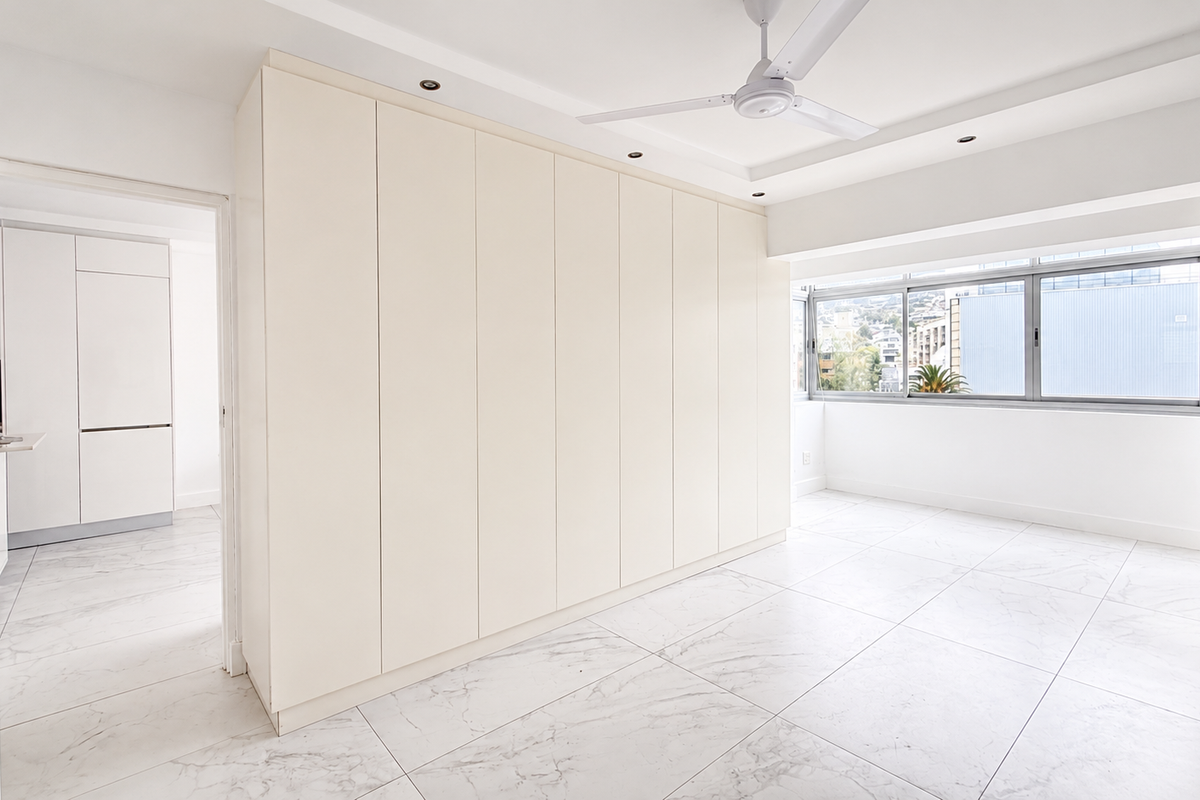 A bright, modern bedroom featuring extensive built-in cupboards, marble-look floor tiles, a ceiling fan, and recessed lighting, offering a clean and neutral living space.