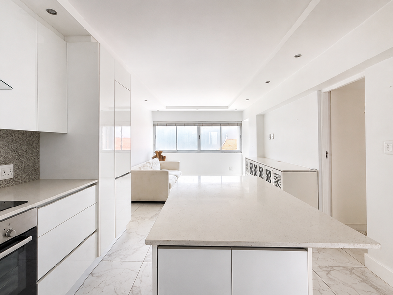 Modern open-plan kitchen and living area featuring a stone island, sleek white cabinetry, integrated appliances, and bright tiled flooring throughout.