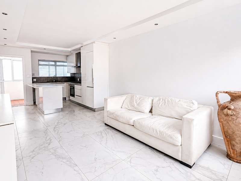 Modern open-plan living area featuring a sleek kitchen with built-in cabinetry, an island, and polished marble-look floor tiles throughout.