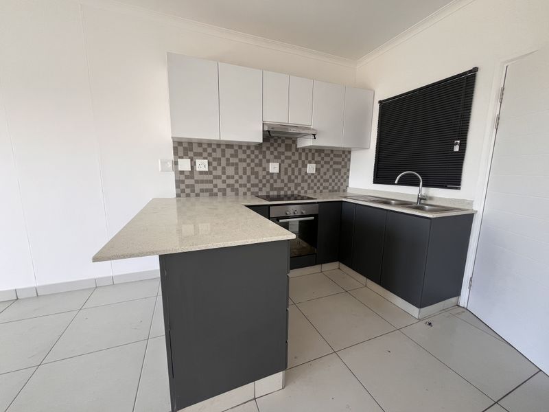 Modern kitchen featuring dark lower cabinets, white upper cabinetry, stone countertops, built-in oven, electric hob, and a tiled backsplash.